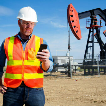 A royalty free image from the oil and gas industry of an oil engineer using a smartphone at a pumpjack to text, make a phone call or surf the internet.